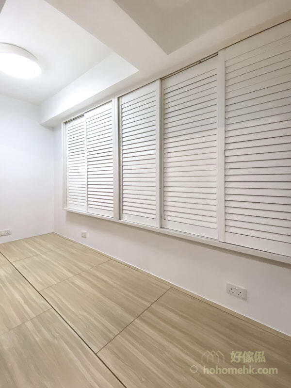 造型俐落的白色木百葉窗簾，能夠完全將不太漂亮的鋁窗框給隔絕在外，再配上純白牆身以及淺木色地台，讓空間瀰漫著一股明淨透亮、寧靜通透之美