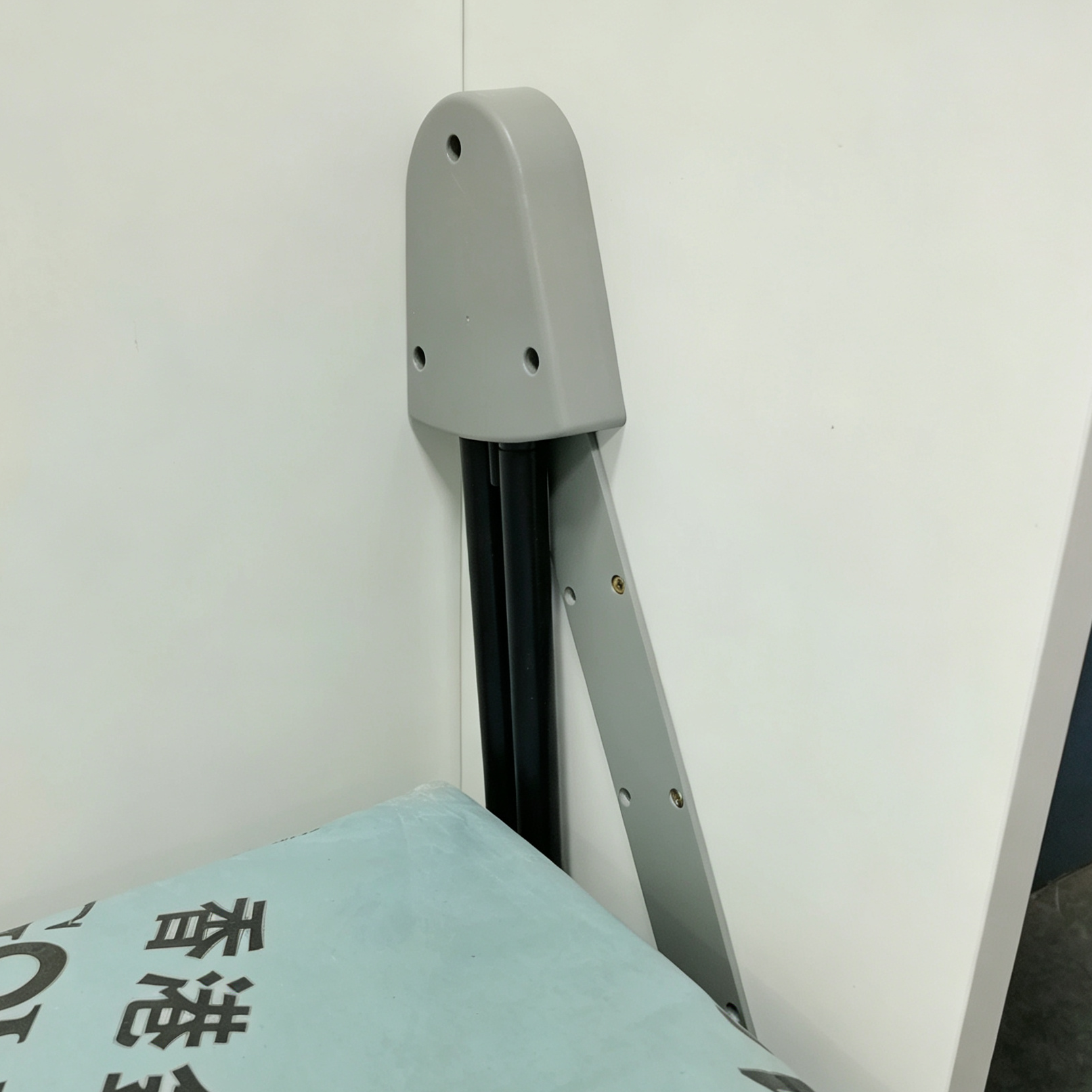 Livo直翻變形床側邊結構近鏡，灰色金屬側臂連住兩條黑色支撐組件，上方接點由圓角灰色護蓋包覆，旁邊係白色櫃板及淺藍床褥。
