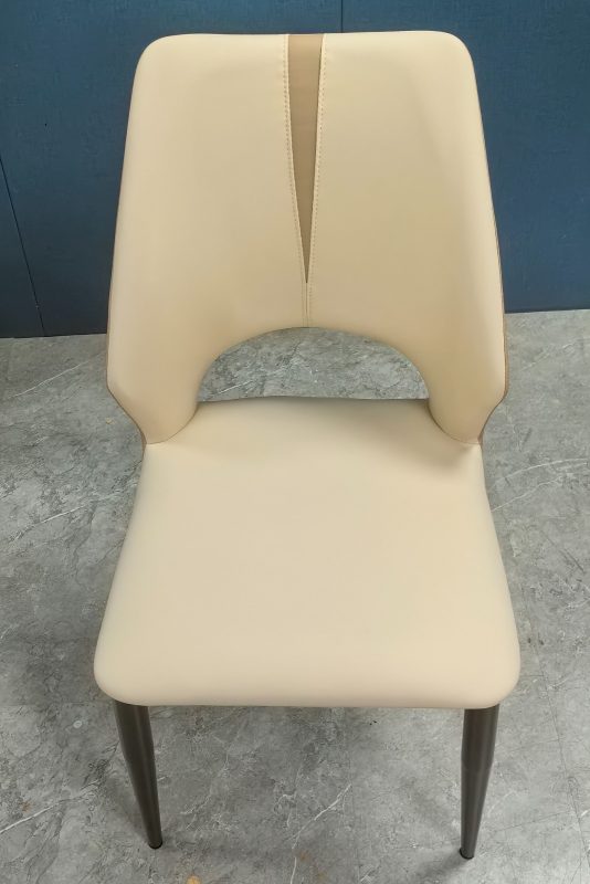 610款餐椅從正面略高角度拍攝，米白色仿皮高背中央加入兩道向下收窄的車線，腰位留有半圓開口，下方連接寬闊圓角坐墊及深灰色金屬椅腳。