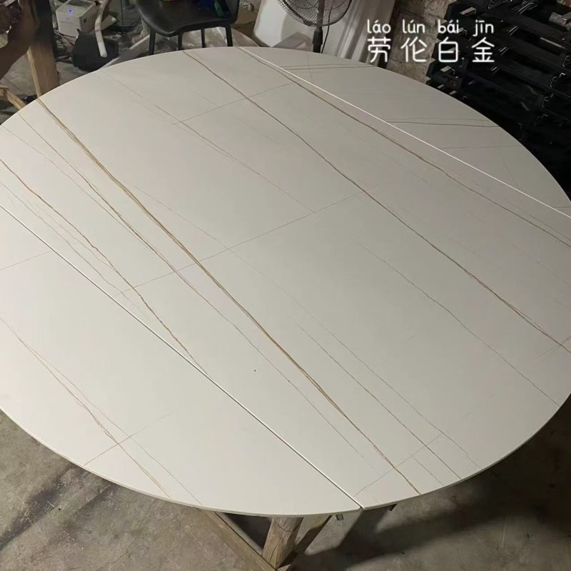 工場內近距離拍攝圓形啞光勞倫白金岩板枱面，米白底色帶金灰色幼紋，多塊拼合枱板由中央伸延至圓邊，枱面正處於圓枱形態。