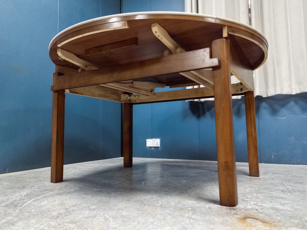 從地面仰拍Camila伸縮餐枱底部，白色岩板枱面下可見木製伸縮路軌、活動承托臂及金屬固定件，四隻胡桃色實木枱腳分立四角。