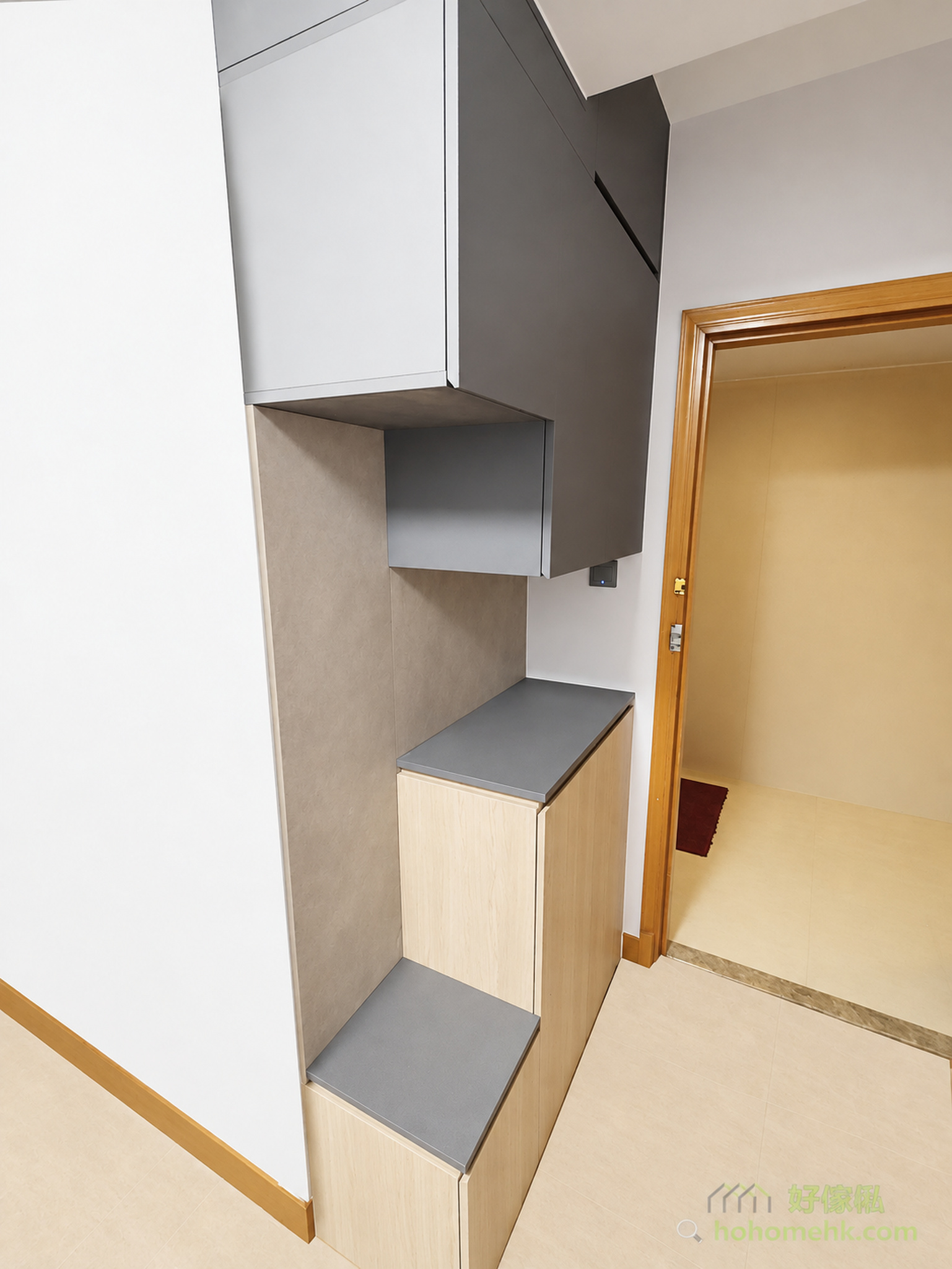 香港玄關訂造鞋櫃連換鞋凳，採用白色高光面板、深灰色翻蓋上櫃與淺木紋下層抽屜，中間設開放式陳列格，下方梯級式灰色坐面換鞋凳緊鄰入口大門，整體設計融合收納、坐墊換鞋及玄關分隔功能於一體。