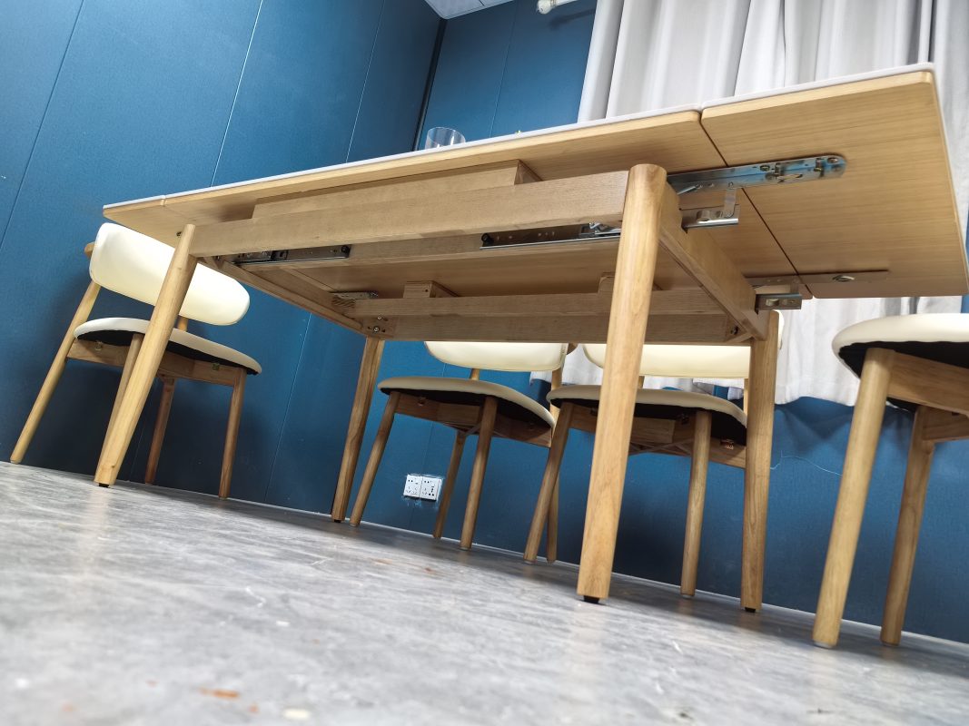 低角度拍攝Reese餐枱其中一側展開，雪山白岩板延伸板向右拉出，枱底金屬路軌、扣件與原木色承托框架清楚可見。
