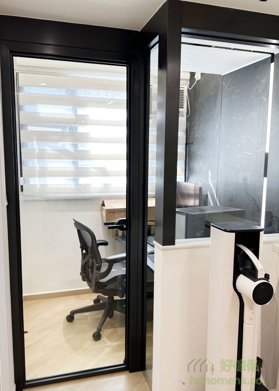 書房的牆身採用了黑色石紋護牆板，與簡約的書桌和高性能電腦設備相得益彰，營造出專業且時尚的工作環境。玻璃間隔的設計既保留了客廳的自然採光，又讓書房保持一定的私密性，實現了美感與功能的平衡。