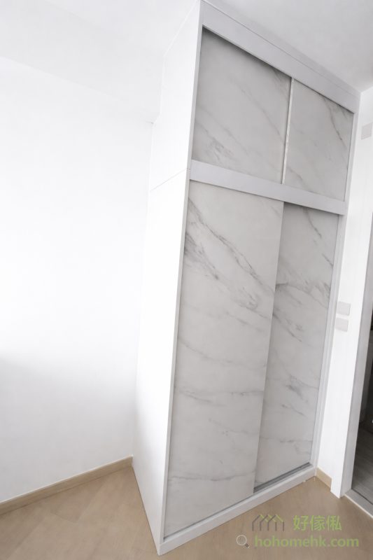 房內的衣櫃亦沿用電視櫃及背景牆的板材及紋理，確保全屋設計風格一致。大理石紋的衣櫃簡約時尚，實用之餘更顯生活品味。這種設計不僅耐看，亦符合現代人對簡約生活的追求。
