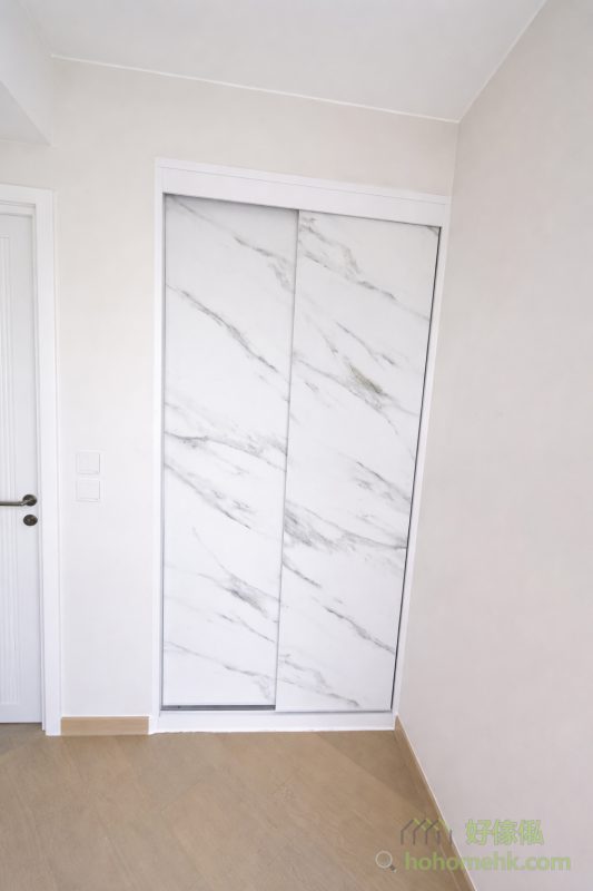 房內的衣櫃亦沿用電視櫃及背景牆的板材及紋理，確保全屋設計風格一致。大理石紋的衣櫃簡約時尚，實用之餘更顯生活品味。這種設計不僅耐看，亦符合現代人對簡約生活的追求。